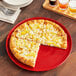 A slice of pizza with pineapple toppings on a red Acopa stoneware plate.