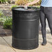 A woman standing next to a Lancaster Table & Seating outdoor trash can with a plastic bottle.