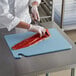 A chef cutting a piece of fish on a blue San Jamar cutting board.