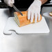 A person cutting bread on a San Jamar white cutting board.