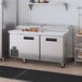 A stainless steel Hoshizaki pizza prep table with two doors on a counter.