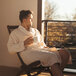 A man in a Telegraph Hill natural twill double layer bath robe sitting in a wooden chair holding a cup of coffee.