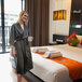 A woman in a Telegraph Hill black twill double layer bath robe standing in a hotel room holding a coffee mug.