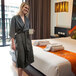 A woman in a Telegraph Hill black kimono robe standing in a hotel room holding a cup.