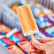 A close-up of a person's hand holding a Blue Ribbon Orange Dream ice cream bar.