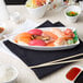 A white porcelain sushi boat with sushi on a table.