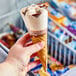 A hand holding a Blue Bunny brownie sundae frozen dessert cone with white and brown ice cream.