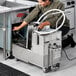 A man using a Fryclone portable fryer oil filter machine on a counter in a professional kitchen.