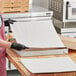 A woman using a Choice white corrugated pizza pad to cut pizza.