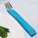 A fork and knife wrapped in a turquoise blue Creative Converting luncheon napkin.