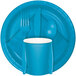 A turquoise blue luncheon napkin with white circles on a blue plate with a fork, spoon, and knife.