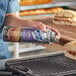 A person spraying a sandwich on a grill with White Cap Grill Release Spray.