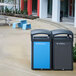 A black Rubbermaid Tailor trash can frame with two blue trash cans on a sidewalk.