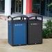 A woman installs a Rubbermaid blue resin decorative recycling panel on two trash cans.