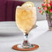 An Acopa customizable glass goblet filled with ice tea and a lemon slice on a coaster.