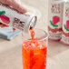 A hand pouring Wild Bill's Craft Beverage Co. Ring Pop Strawberry Soda from a can into a glass with ice.