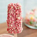 A hand holding a pink and white strawberry shortcake bar with Yum Crumbs on it.