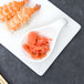 A white plate with sushi and shrimp on it with a white porcelain tapas spoon.
