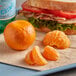 Fresh Clementines on a tray with a sandwich and peeled orange fruit.