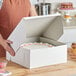 A woman holding a Baker's Lane white cake box with a cake inside.