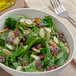 A bowl of fresh baby spinach salad with nuts and raisins on a table with a fork.