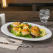 A Libbey white porcelain platter with a lemon wedge on it, with a fork and knife on a napkin.