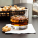 A Libbey rocks glass of whiskey on the rocks with peanuts on the side.