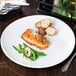 A Libbey Porcelana bright white round porcelain coupe plate with a piece of salmon and green beans on a table.