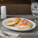 A bagel with cream cheese and vegetables on a Libbey Porcelana white oval platter.