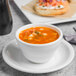 A Libbey Porcelana bright white porcelain bouillon bowl with soup on a plate.