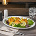 A Libbey Porcelana white oval platter with food and a lemon slice.