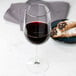 A Libbey tall wine glass filled with red wine next to a plate of pastries on a marble table.