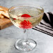 A Libbey Hobstar coupe cocktail glass with liquid and a cherry in it.