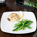 A Libbey Porcelana square porcelain coupe plate with food including green beans and a lemon on a table.