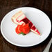 A slice of cheesecake with strawberries on a Libbey Porcelana white coupe plate.