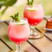 Two glasses of pink drinks made with Andros Chef Sweetened Lychee Puree on a table with lime and mint leaves.
