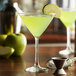 A Libbey martini glass filled with green liquid with a slice of green apple on the rim.