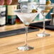 A clear Libbey Vina 8 oz. martini glass with a stem, shown with olives and being filled with liquid.