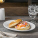 A Libbey white oval porcelain platter with a bagel sandwich on it.