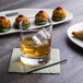 A Reserve by Libbey Modernist Rocks glass with brown liquid and ice on a table next to a plate of food.