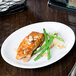 A Libbey Bright White oval coupe platter with a piece of fish and green beans on a table.