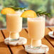 Two glasses of peach smoothie with a slice of peach on top of a table.
