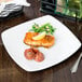 A Libbey Porcelana square white porcelain coupe plate with food on a table.