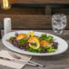 A Libbey white porcelain platter with a plate of food, a lemon wedge, and a silver fork.