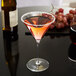 A Reserve by Libbey Renaissance martini glass with pink liquid and grapes on a black surface.