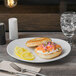 A Libbey Porcelana bright white porcelain plate with a bagel and salmon with lemon slices.