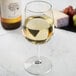 A Libbey Vina wine glass filled with white wine on a marble table with grapes and cheese.