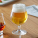 A Reserve by Libbey Belgian beer glass full of beer with foam on a table.