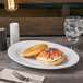 A Libbey white porcelain platter with a bagel, salmon, and onions on a table.