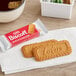 A red and white package of Lotus Biscoff cookies on a napkin next to a cup of coffee.